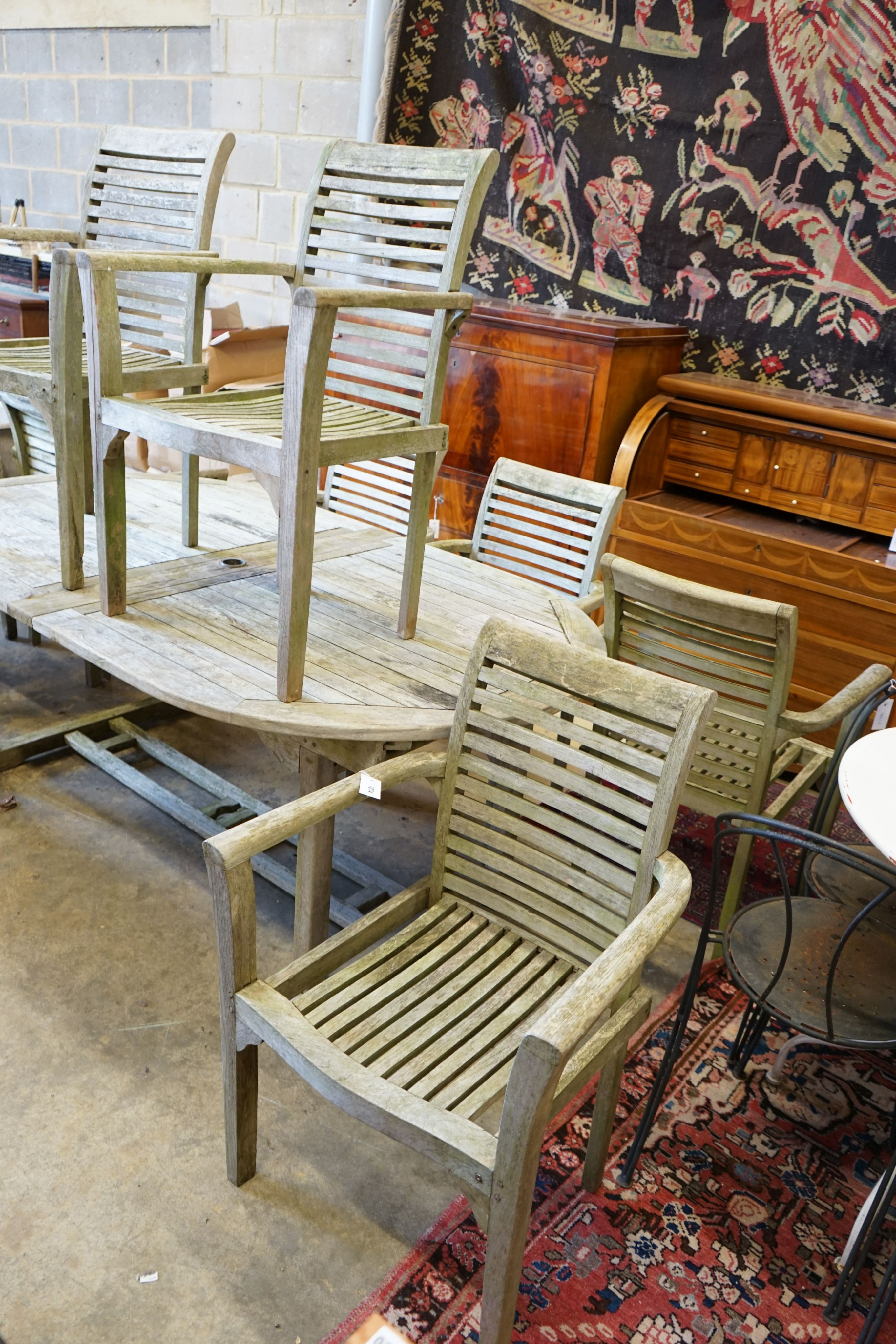 A weathered teak extending oval garden table, length 196cm, width 110cm, height 75cm and eight weathered teak elbow chairs